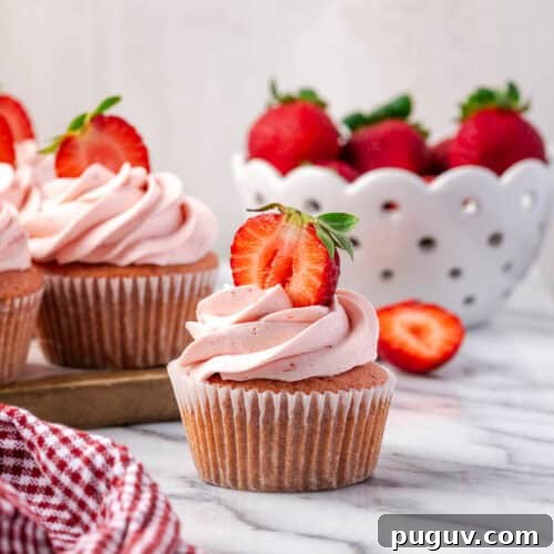 A strawberry cupcake decorated with pink frosting sitting on a marble counter.