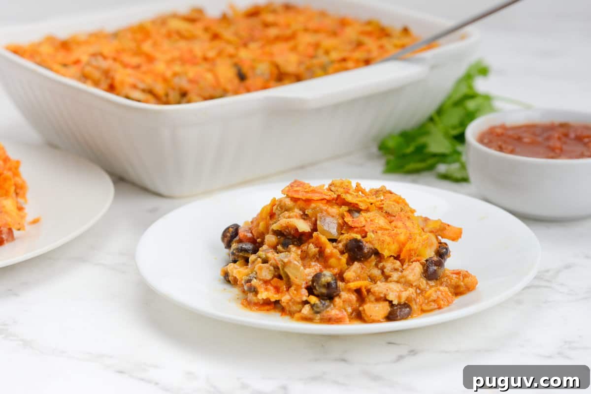 Doritos Casserole Recipe with WW SmartPoints and Tips 14 A small white plate is filled with a serving of Doritos Casserole. The baking dish and a small bowl of salsa are shown behind the plate.