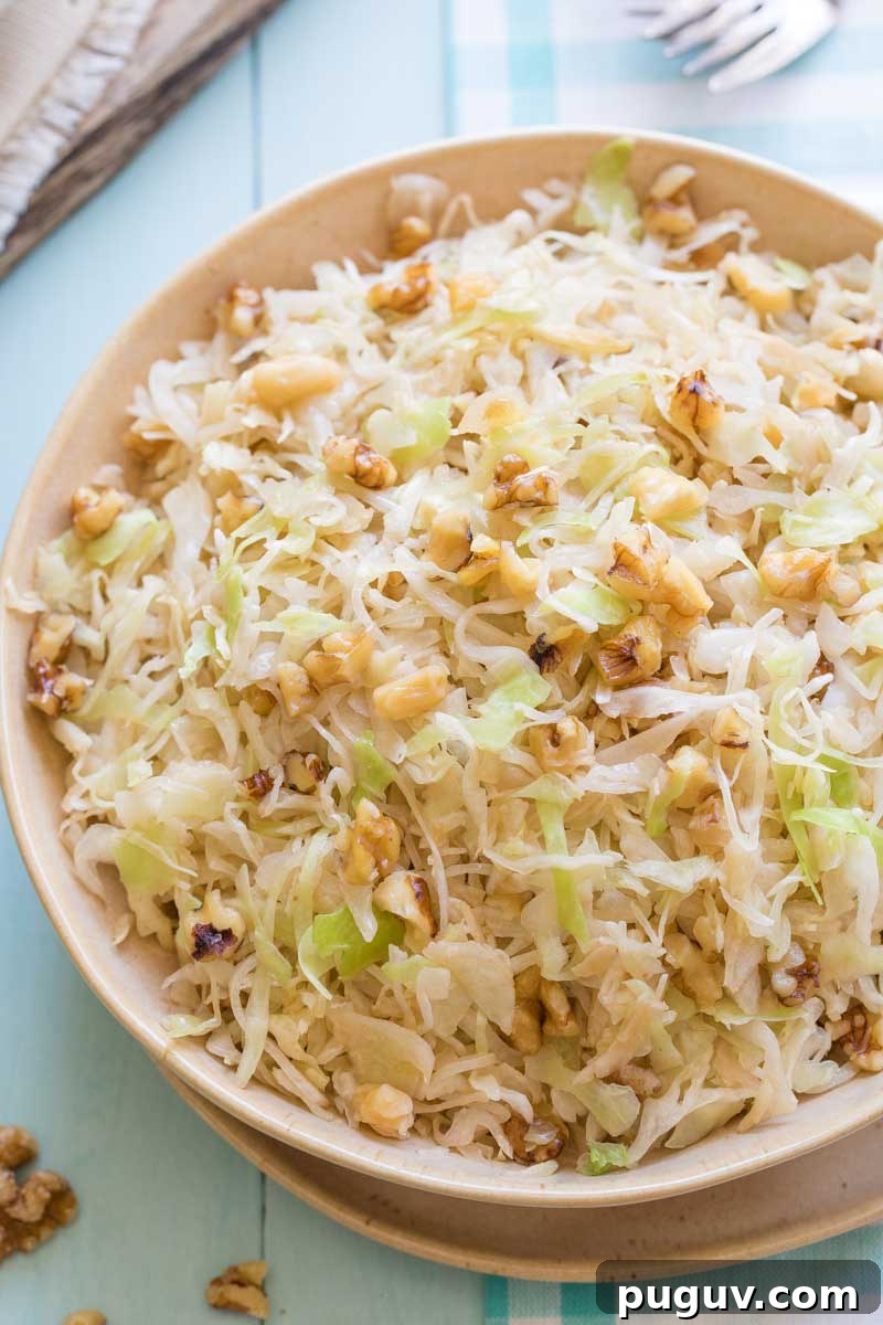 Brown Butter Sautéed Cabbage with Toasted Walnuts 2 Overhead closeup of tan serving bowl of sauteed cabbage on light blue background and cloth, garnished with extra nuts.