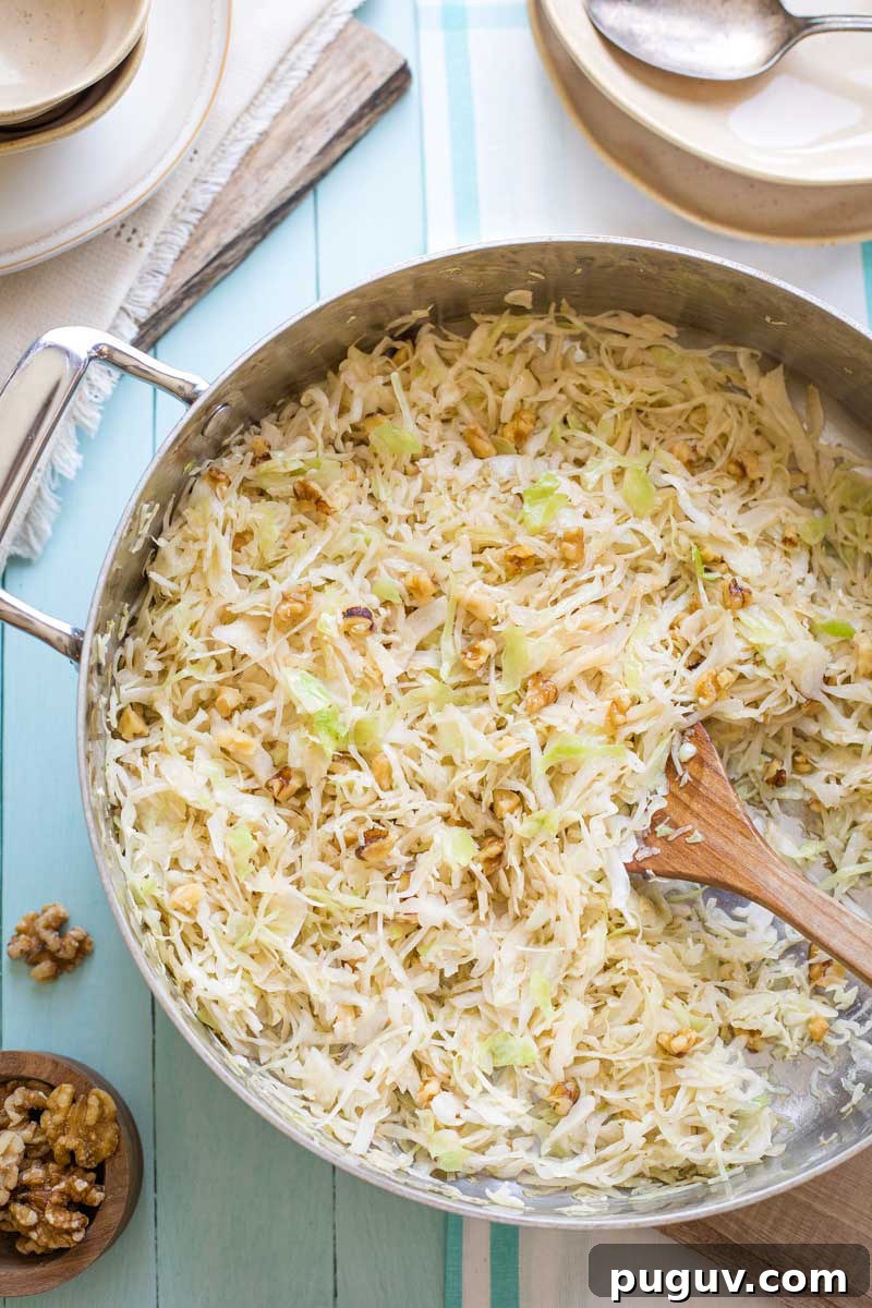 Brown Butter Sautéed Cabbage with Toasted Walnuts 8 Overhead of saute pan full of finished, cooked cabbage on blue background with plates and utensils ready to serve.