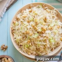Brown Butter Sautéed Cabbage with Toasted Walnuts 11 Overhead of serving bowl full of cooked cabbage on light blue background, with serving items and extra nuts near.