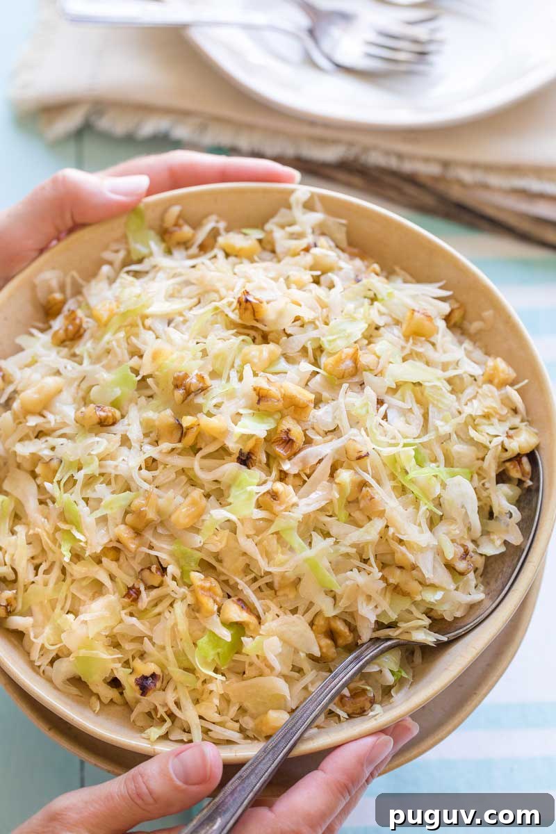 Brown Butter Sautéed Cabbage with Toasted Walnuts 4 Two hands holding serving bowl with serving spoon tucked in, with forks and plates in background below.