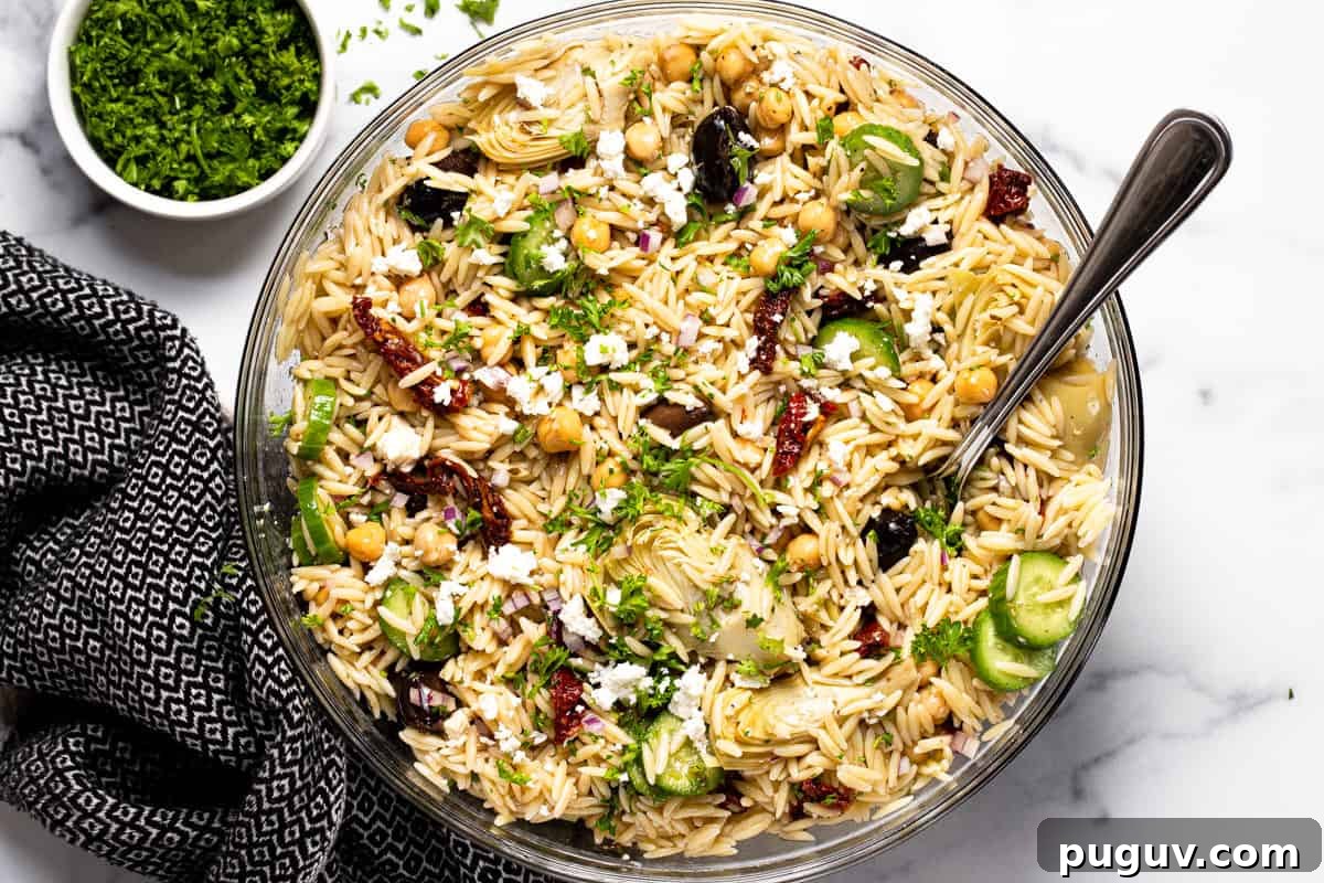 20-Minute Greek Orzo Salad with Feta & Olives 8 Large glass bowl filled with Greek pasta salad garnished with parsley