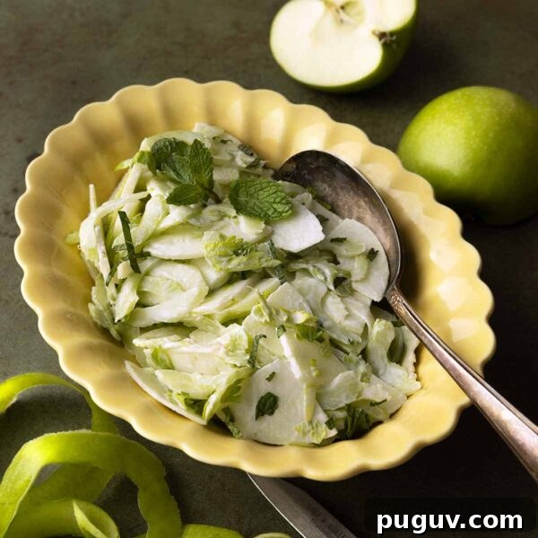 An apple and celery salad in a creamy dressing, garnished with mint leaves in a yellow scalloped bowl.