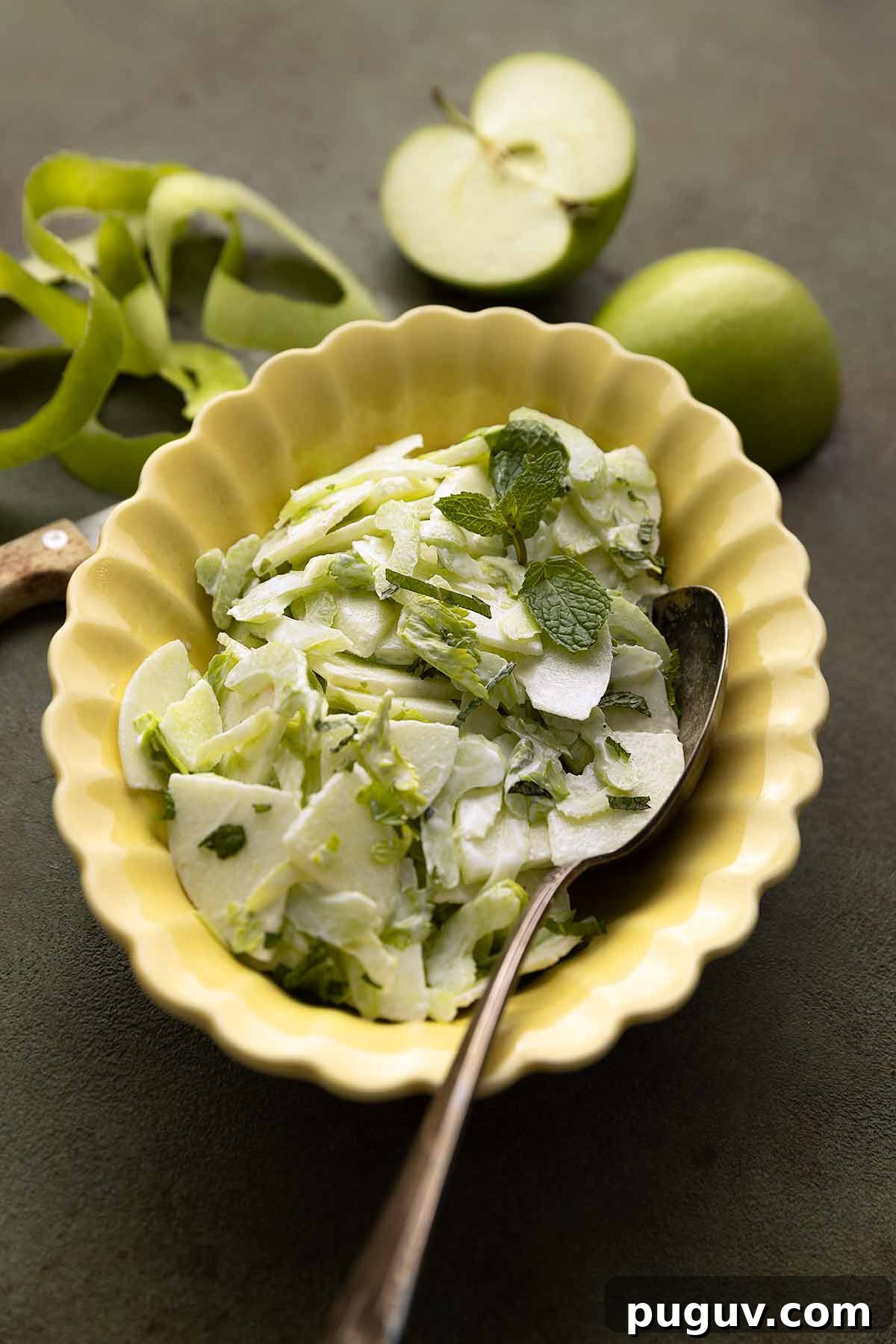 An apple and celery salad in a creamy dressing, garnished with mint leaves in a yellow scalloped bowl.