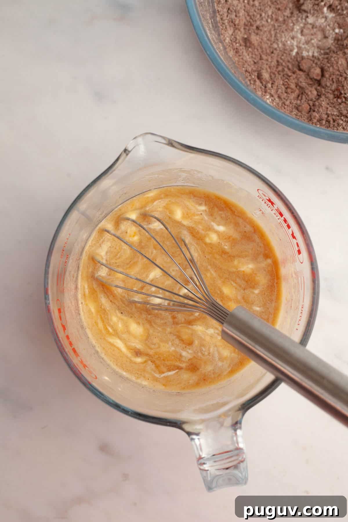 A jug with a whisk and a light brown mixture in it.