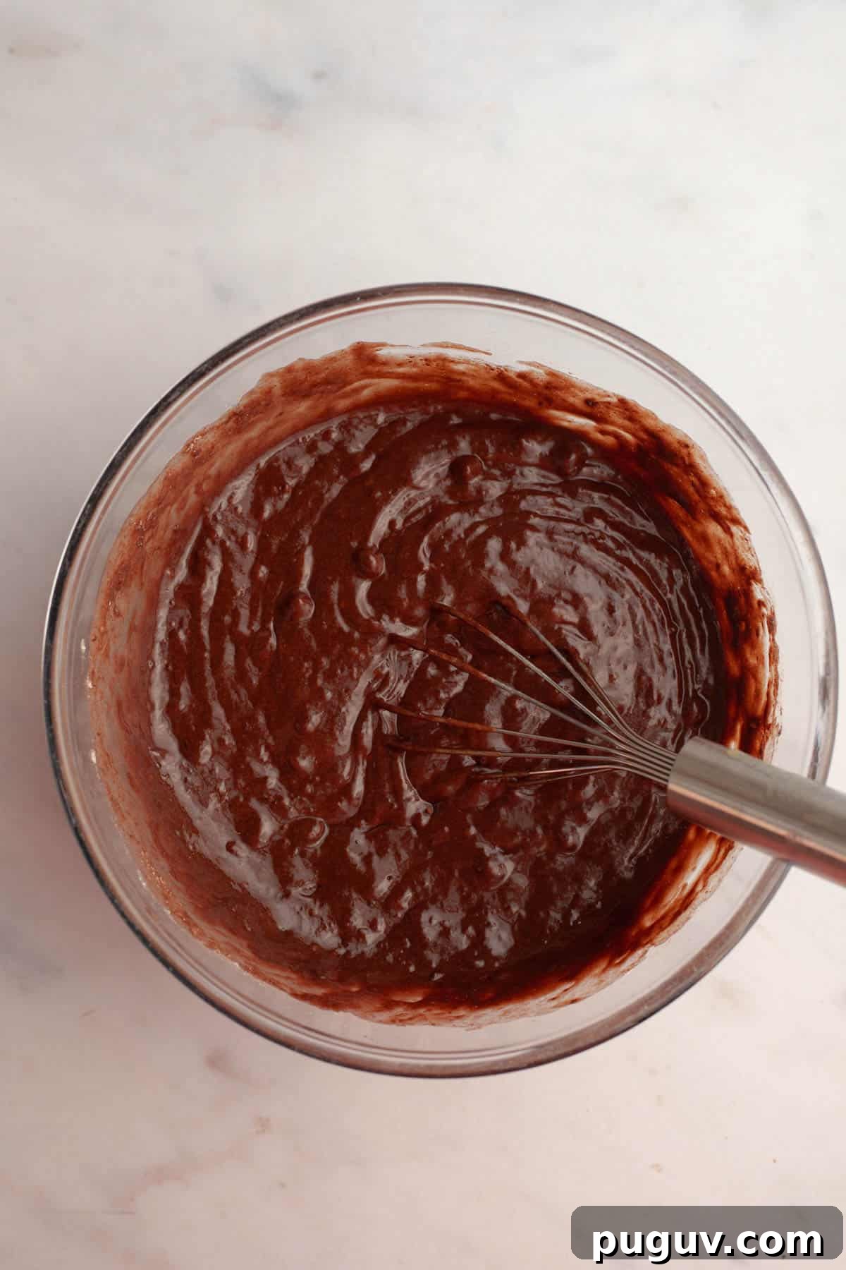 A glass bowl with chocolate cake batter in it.