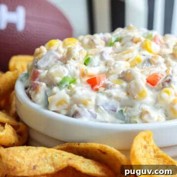 Cold corn dip in a white bowl surrounded frito scoops.