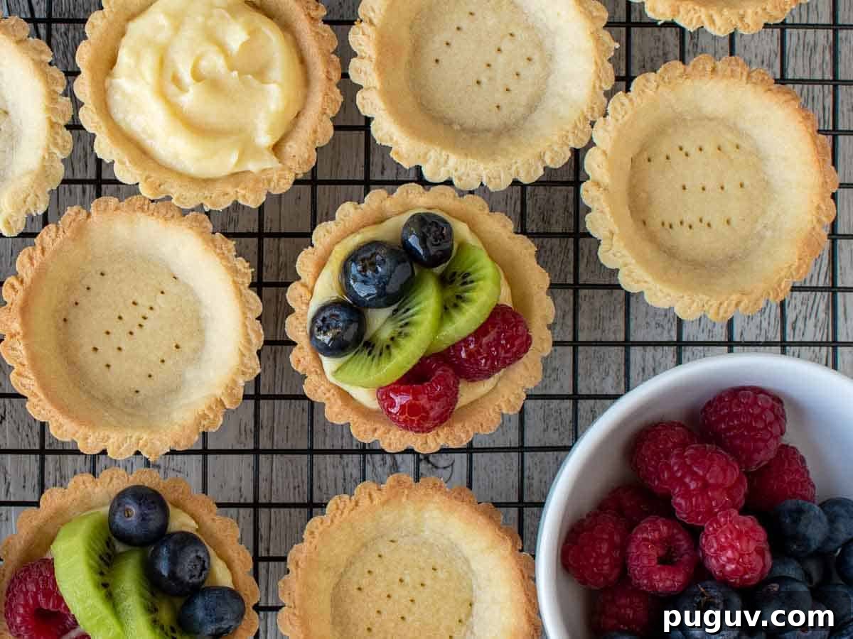 Overhead view of mini tarts, some empty, some filled with pastry cream and some topped with berries and sliced kiwi fruit.