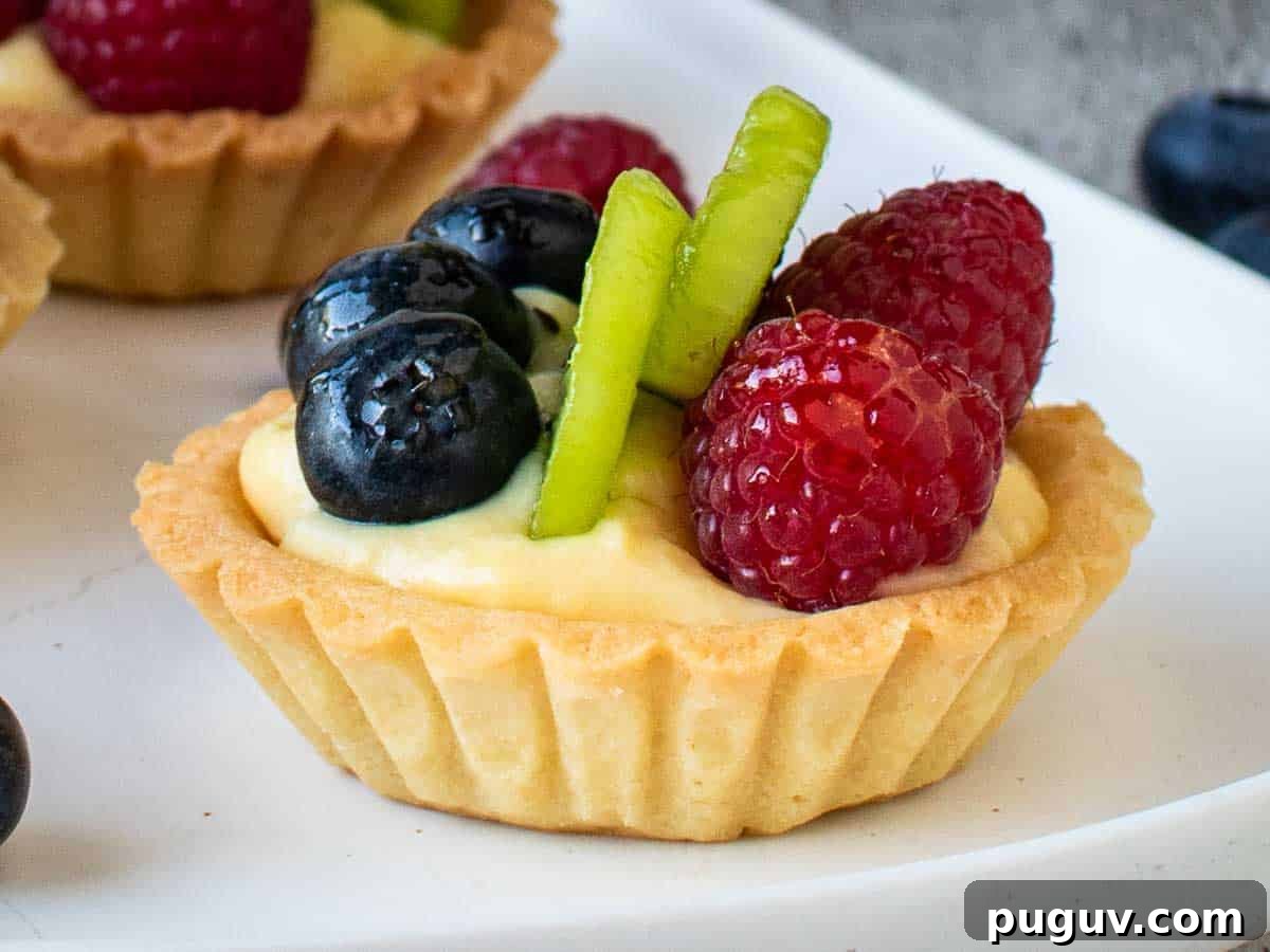 Close up of fluted tart filled with pastry cream and topped with blueberries, sliced kiwi fruit and raspberries