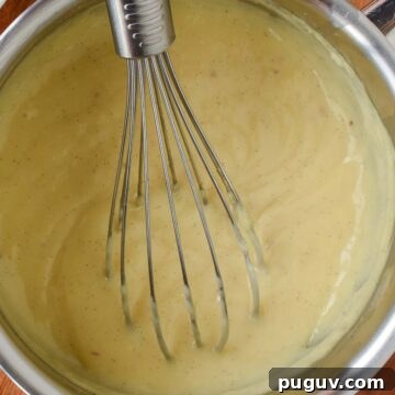 Overhead view of thickened pastry cream in a saucepan with a whisk.