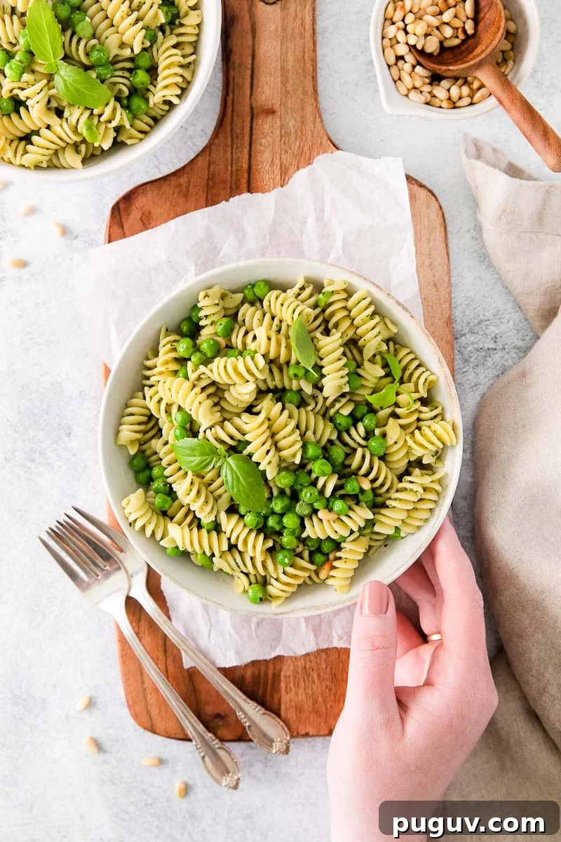 Creamy Pea Pasta with Garlic and Parmesan 8 a hand holding a plate of rotini pasta salad with green vegetables and silverware beside the plate.
