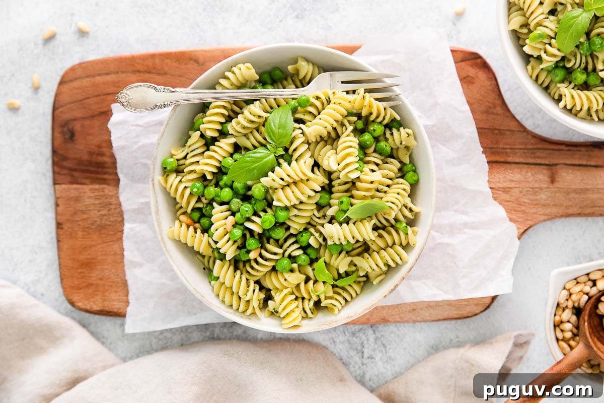 Creamy Pea Pasta with Garlic and Parmesan 9 Bowl of pesto pasta with veggies on top of a wooden board.