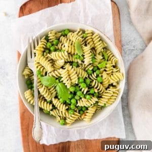 Creamy Pea Pasta with Garlic and Parmesan 10 Fork in a serving bowl of pesto pasta with veggies, garnished with fresh basil.
