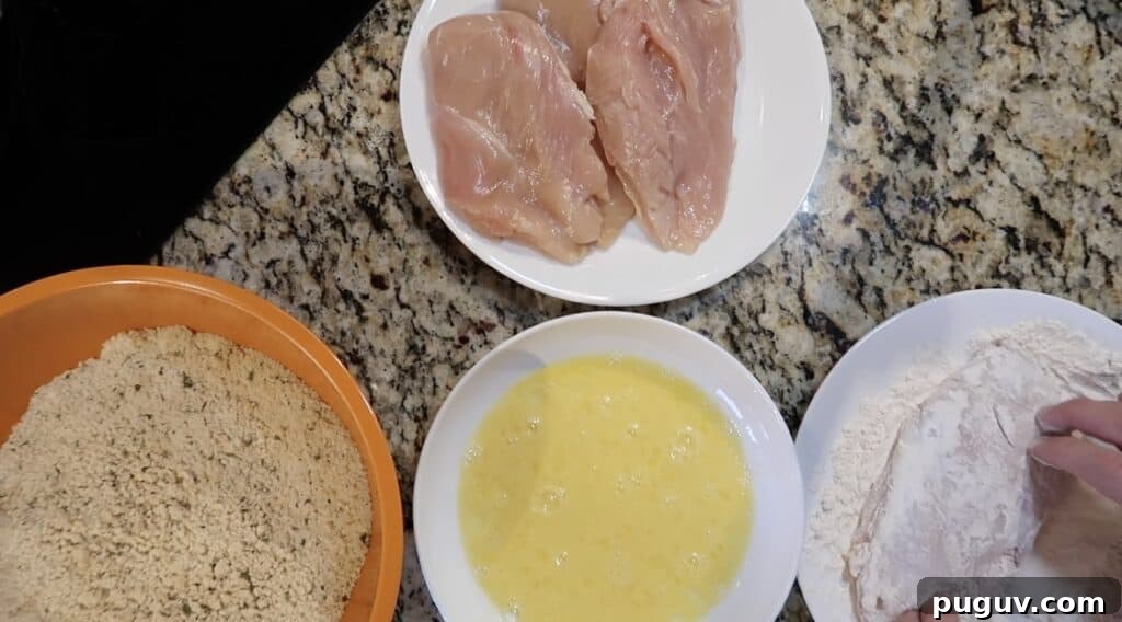 4 stations: chicken cutlets, flour, beaten egg, and Panko breadcrumb mixture. One cutlet is being dredged in the flour