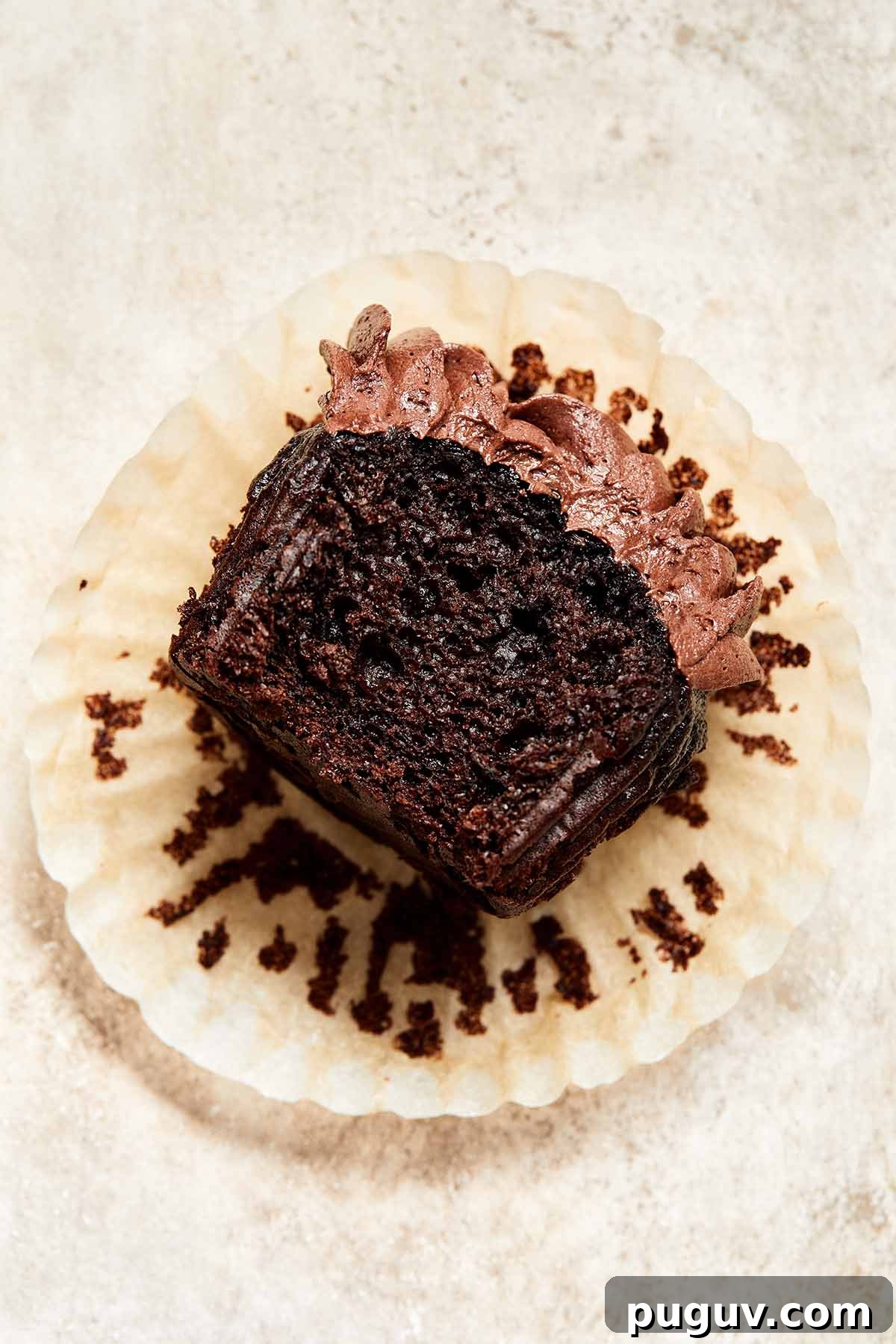 Moist Chocolate Zucchini Cupcakes with Fudgy Cocoa Glaze 2 Chocolate cupcake on a cupcake wrapper with a bite taken out of it.
