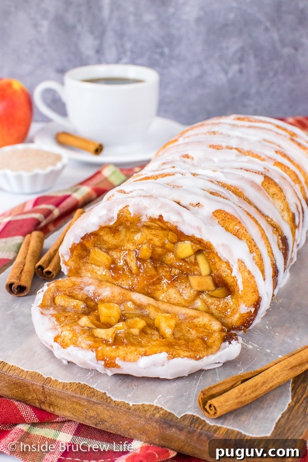 Apple Cinnamon Pull Apart Bread - this gooey pull apart bread is filled with cinnamon apples and drizzled with a sweet glaze. It is a delicious recipe to make for breakfast or brunch this fall. A wood board with a loaf of apple cinnamon pull apart bread drizzled with glaze and one sliced falling forward