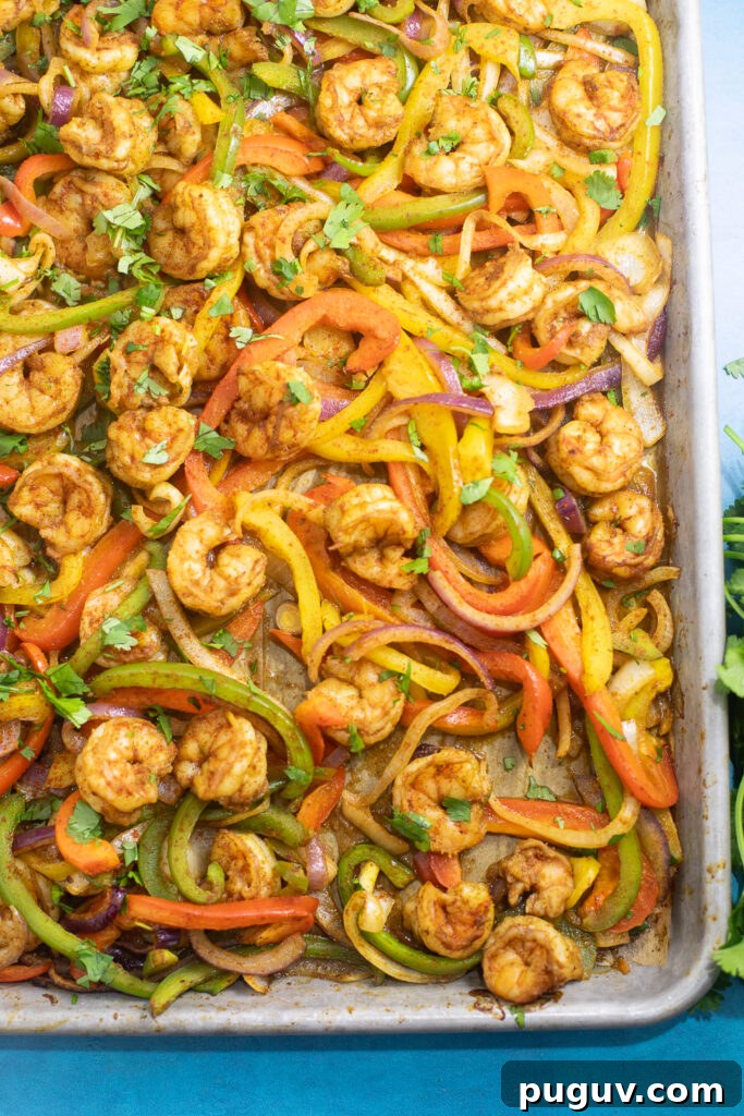 Sheet Pan Shrimp Fajitas Recipe for Quick Weeknight Dinners 3 Overhead view of a sheet pan lined with parchment paper and loaded with shrimp, bell pepper strips, and onion.