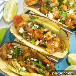 Sheet Pan Shrimp Fajitas Recipe for Quick Weeknight Dinners 5 Overhead view of three sheet pan shrimp fajitas in corn tortillas topped with fresh cilantro, queso fresco, and avocado slices, and surrounded by lime wedges.