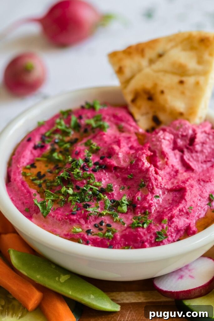 Creamy Beet Hummus Recipe: Vibrant Homemade Dip 2 Pink beet hummus in a small white bowl surrounded by vegetables for dipping.