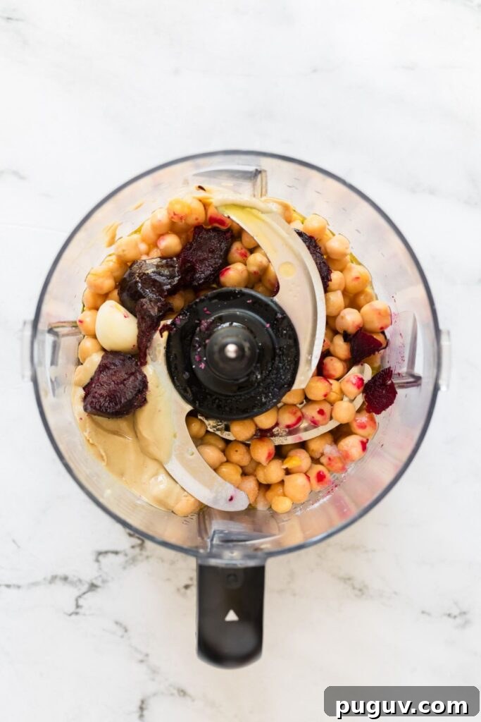 Creamy Beet Hummus Recipe: Vibrant Homemade Dip 5 Roasted beets and other ingredients in a food processor before mixing on a marble table.