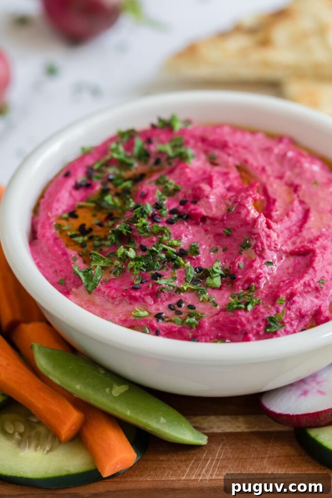 Creamy Beet Hummus Recipe: Vibrant Homemade Dip 7 Bright pink hummus in a small white bowl surrounded by veggies.