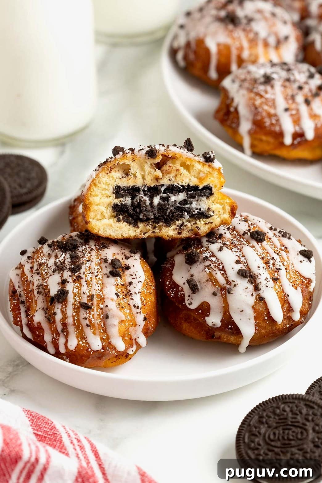 A white rimmed plate holding three fried cinnamon rolls with Oreos in the middle. The one of top is cut open to reveal the oreo inside.
