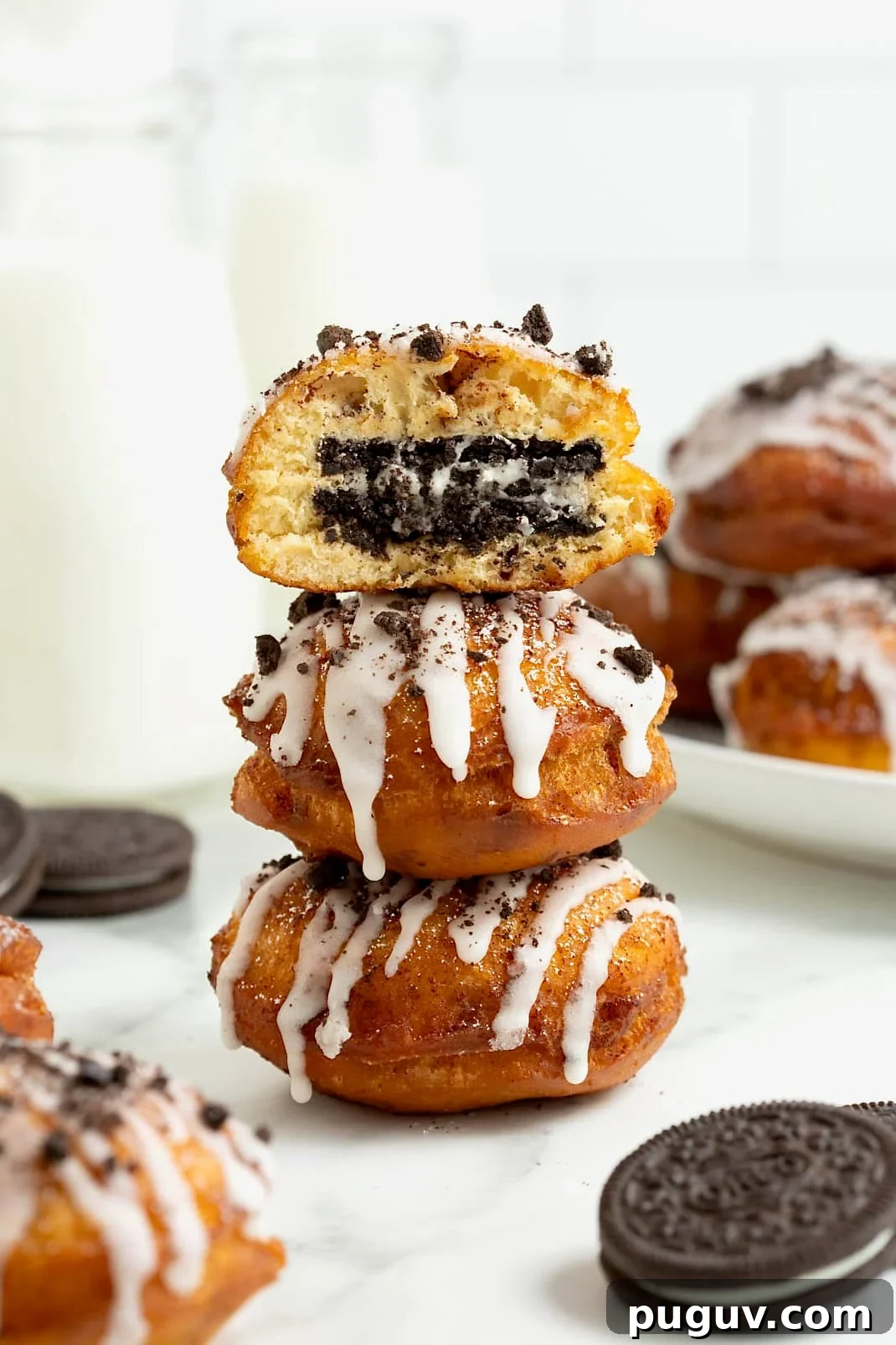 A stack of three cinnamon roll fried Oreos on a white marble counter. The top fried Oreo has a bite out of it revealing the Oreo inside.