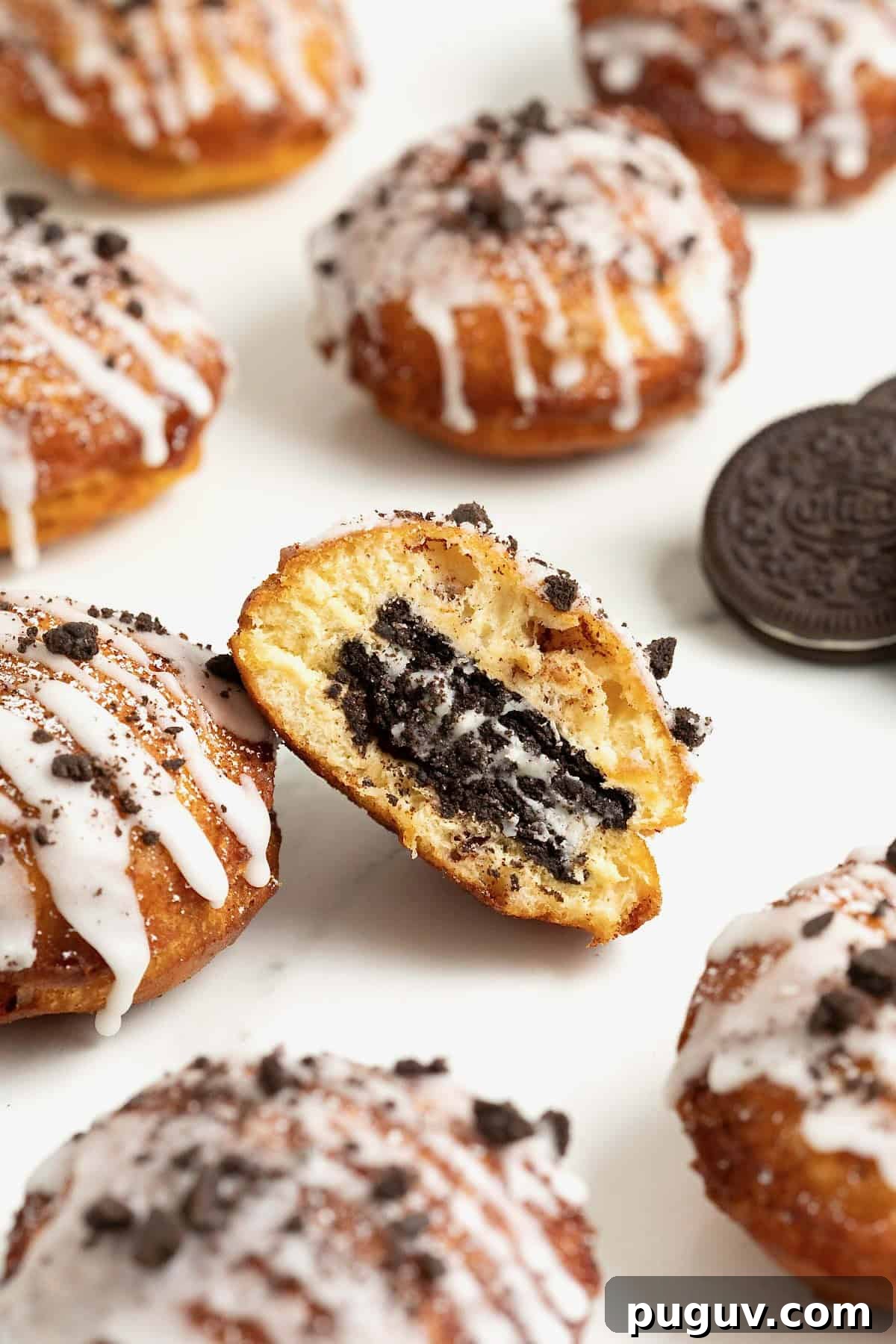 Six cinnamon roll fried Oreos on a white marble counter. The center one is cut in half to show the Oreo inside.
