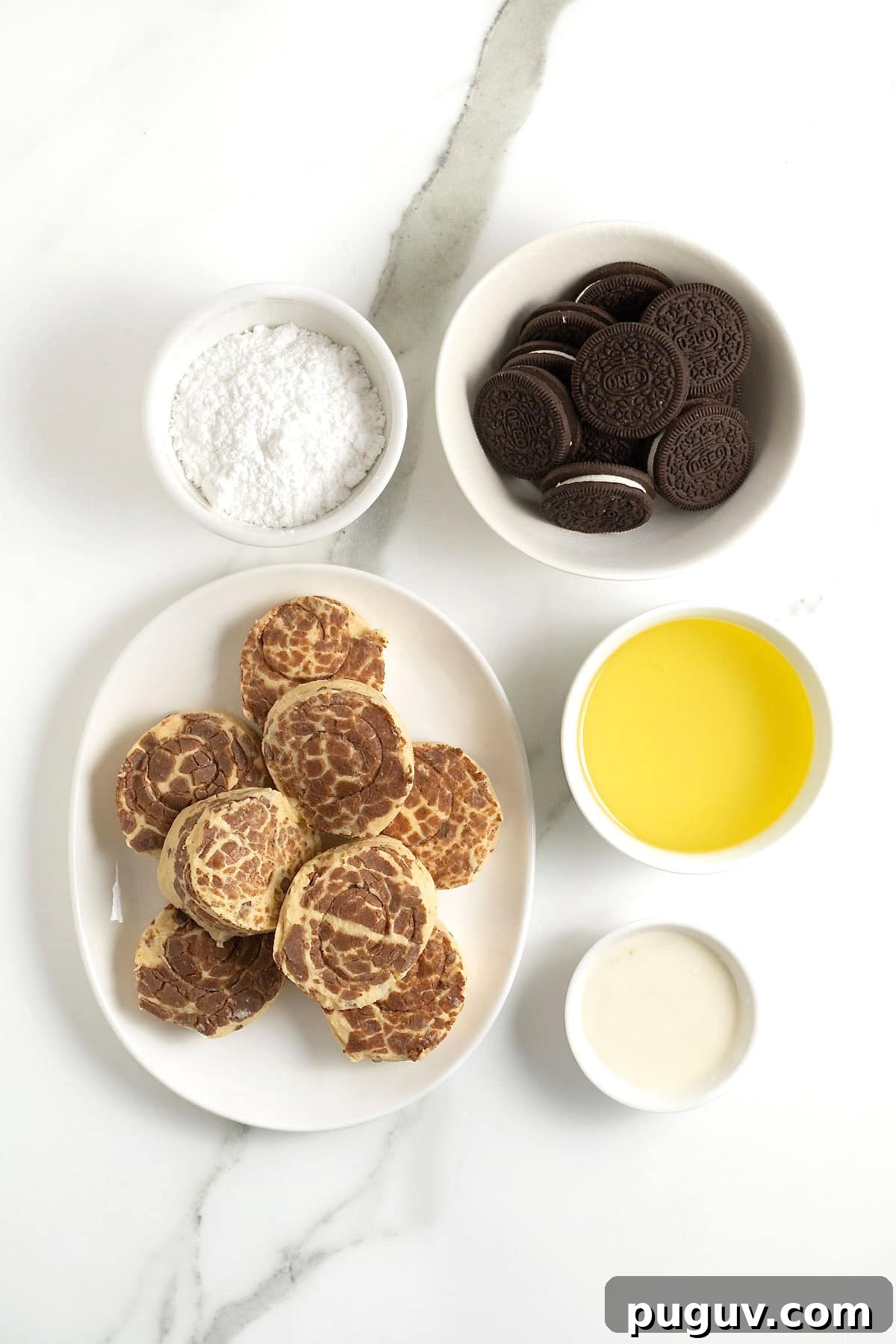ingredients to make cinnamon roll deep fried Oreos in small white dishes on a white marble counter.