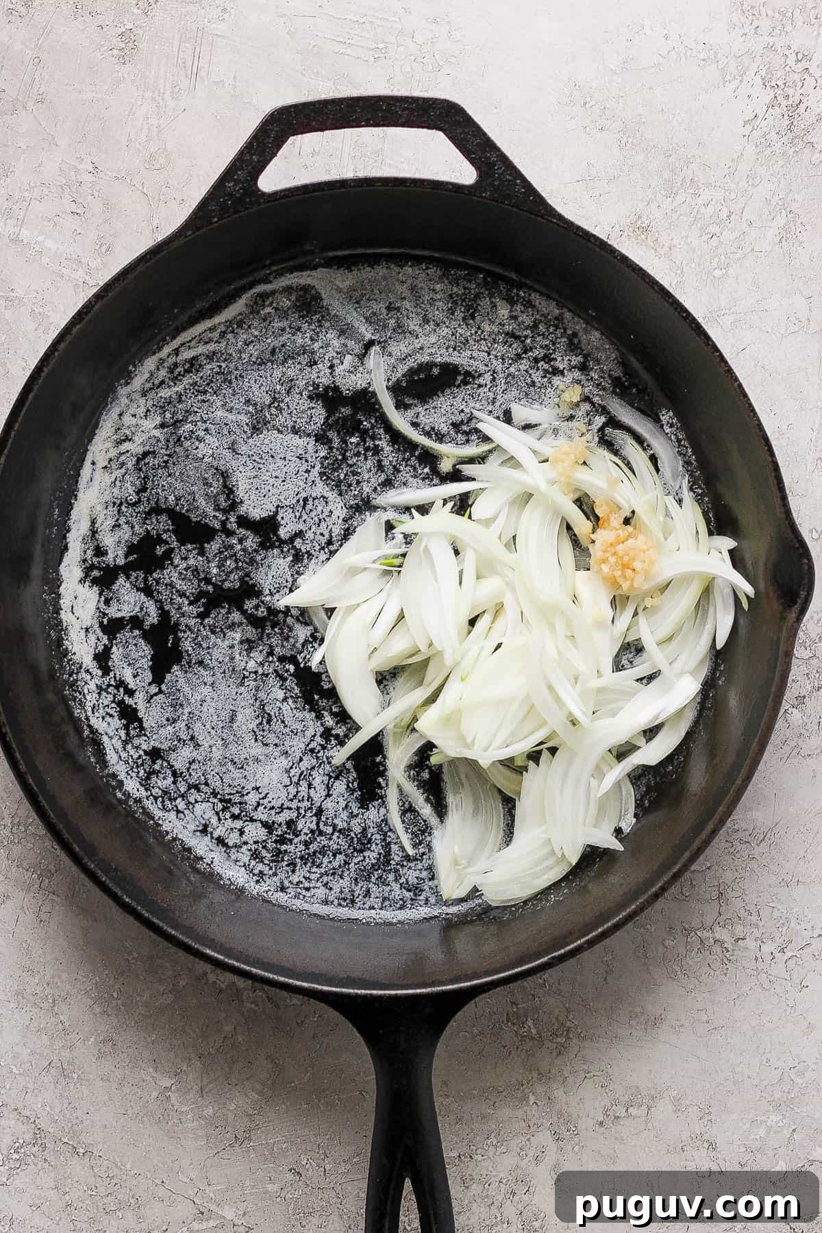 A cast iron skillet with melted butter, with onions and garlic added to the pan.