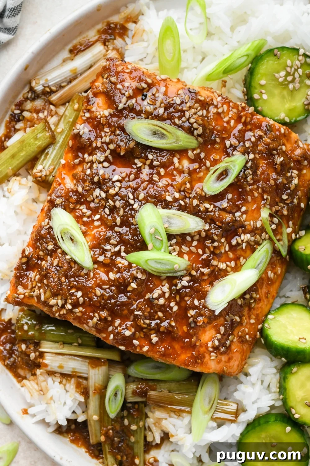 30-Minute Garlic-Ginger Glazed Salmon Recipe (Gluten-Free) 2 Baked garlic ginger salmon garnished with freshly sliced green onion, on top of white rice, next to a serving of sesame cucumber salad.