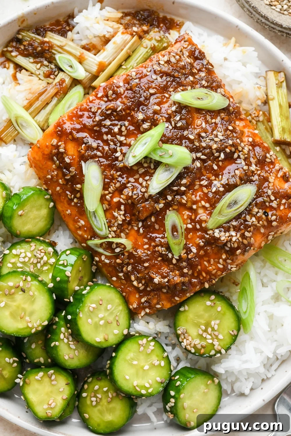 30-Minute Garlic-Ginger Glazed Salmon Recipe (Gluten-Free) 13 Baked garlic ginger salmon garnished with freshly sliced green onion, on top of white rice, next to a serving of sesame cucumber salad.