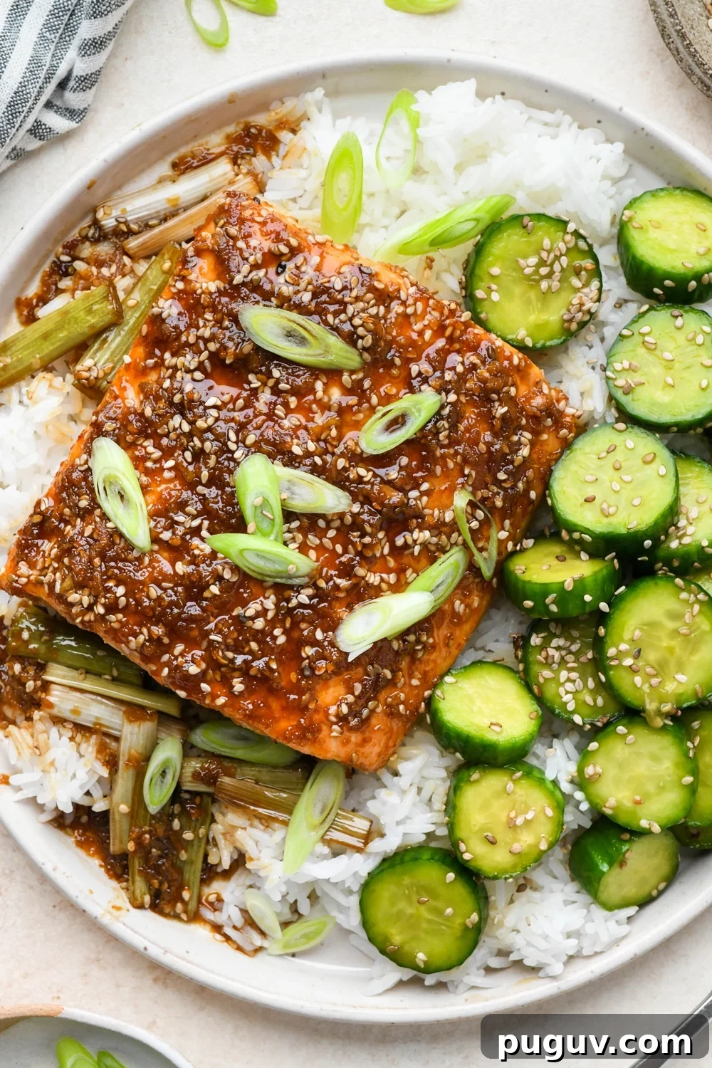 30-Minute Garlic-Ginger Glazed Salmon Recipe (Gluten-Free) 6 Baked garlic ginger salmon garnished with freshly sliced green onion, on top of white rice, next to a serving of sesame cucumber salad.
