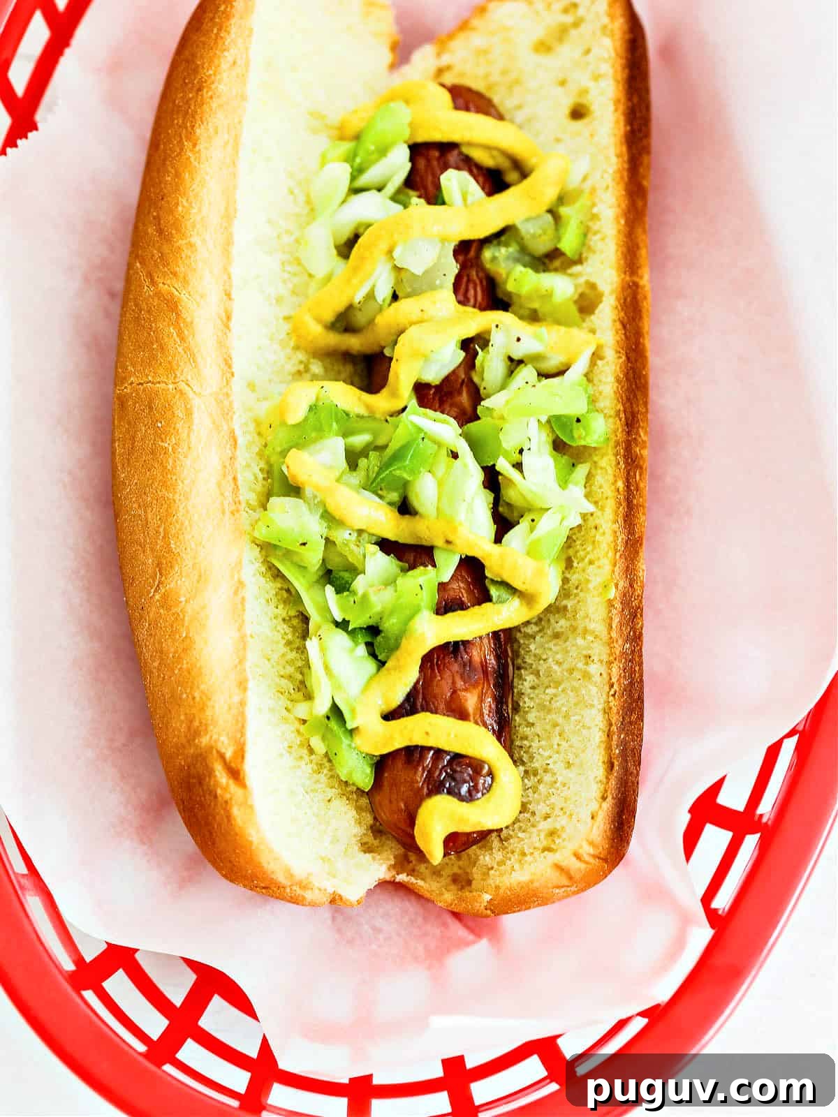 A hot dog with toppings in a red plastic basket lined with paper.