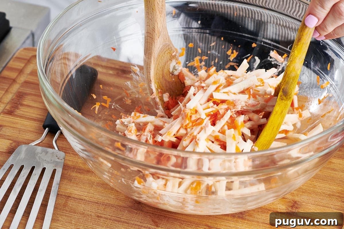 How to Cook Celeriac: Simple Techniques and Delicious Recipes 9 Woman tossing Carrot Celeriac Remoulade in a bowl.