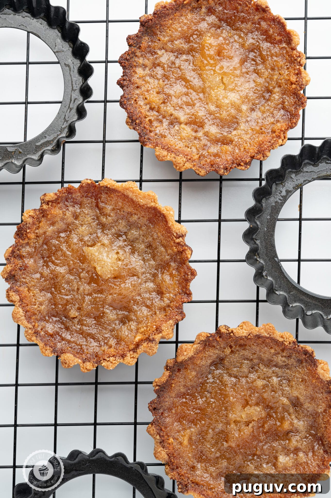 Sugar-Free Butter Tarts: Low-Carb Keto & Gluten-Free Recipe 3 Sugar-free butter tarts cooling a black cooling rack with the metal tart pans scattered around.
