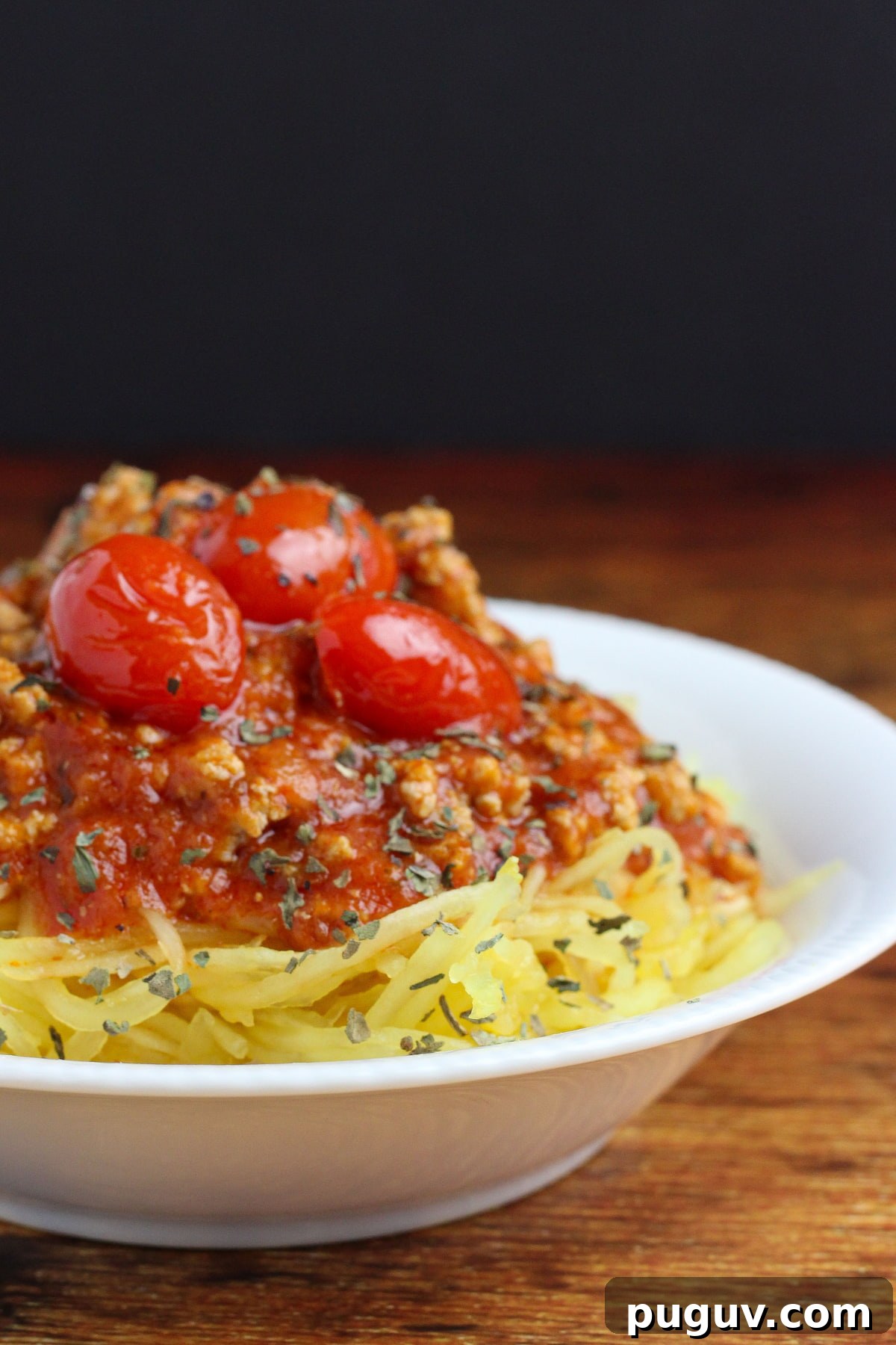 paleo spaghetti squash - in a white bowl, ready to eat and topped with meat sauce and cherry tomatoes