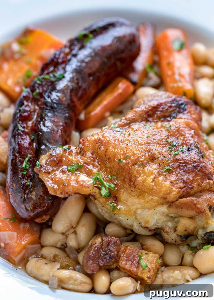 This comforting French Cassoulet recipe has juicy chicken, sausage, bacon and white beans that simmer away in a broth spiked with onion, garlic and herbs. #casserole #dinner #French #cassoulet roasted sausage and chicken with white beans