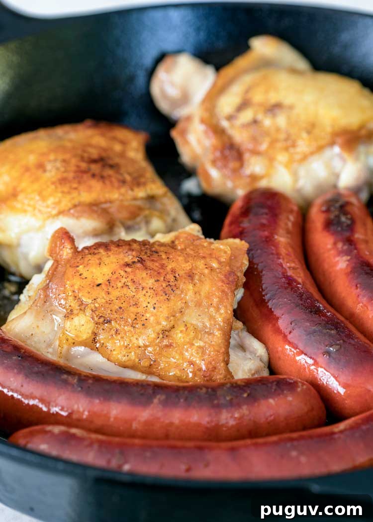 This comforting French Cassoulet recipe has juicy chicken, sausage, bacon and white beans that simmer away in a broth spiked with onion, garlic and herbs. #casserole #dinner #French #cassoulet pan fried sausages and chicken thighs