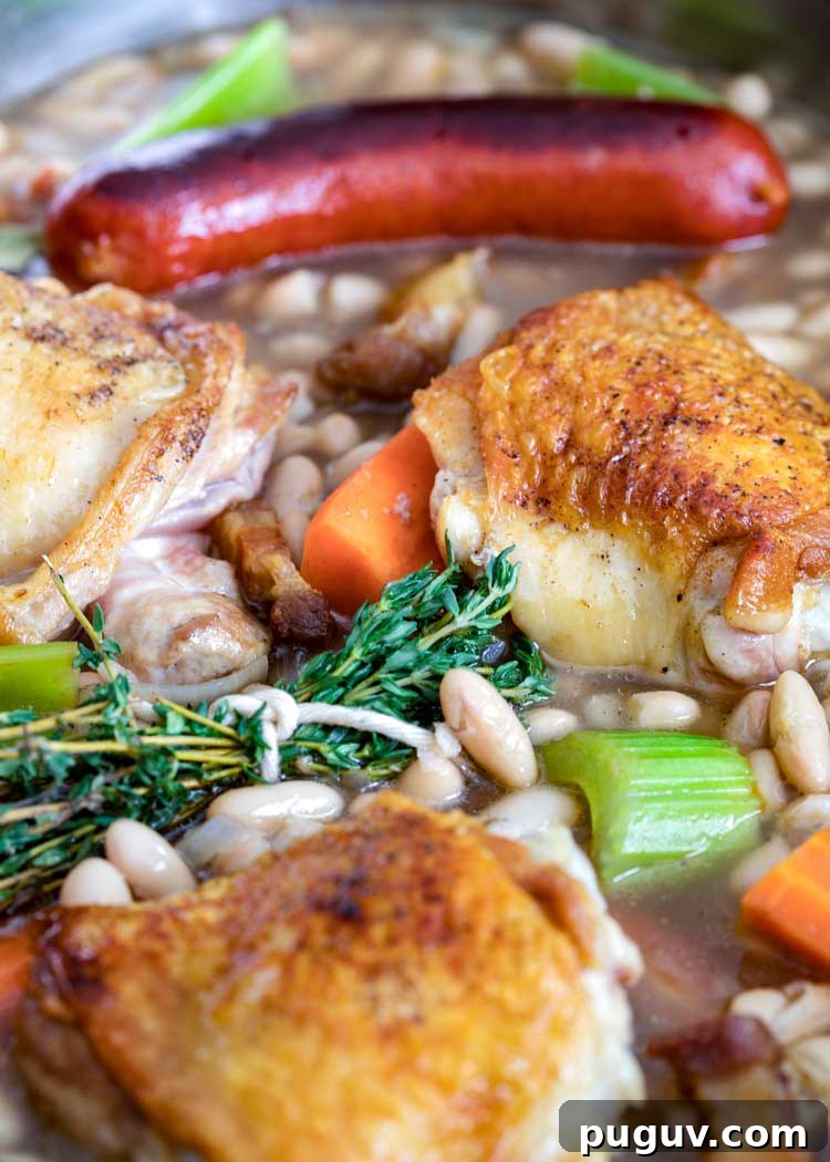 This comforting French Cassoulet recipe has juicy chicken, sausage, bacon and white beans that simmer away in a broth spiked with onion, garlic and herbs. #casserole #dinner #French #cassoulet thyme bundle with chicken and sausages