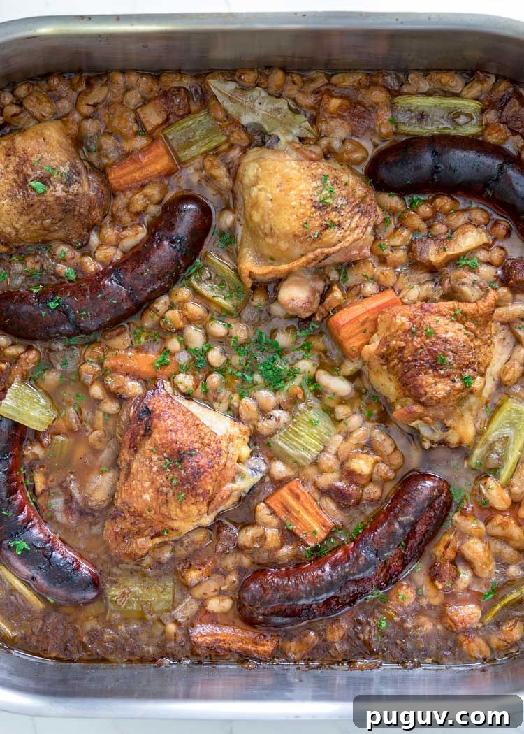 This comforting French Cassoulet recipe has juicy chicken, sausage, bacon and white beans that simmer away in a broth spiked with onion, garlic and herbs. #casserole #dinner #French #cassoulet over head shot of roasted sausages, chicken and whte beans