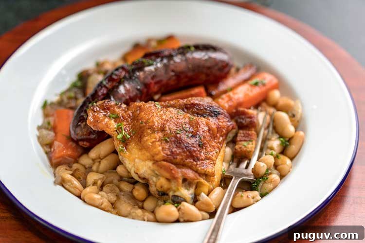 This comforting French Cassoulet recipe has juicy chicken, sausage, bacon and white beans that simmer away in a broth spiked with onion, garlic and herbs. #casserole #dinner #French #cassoulet plate of Easy French Cassoulet Recipe