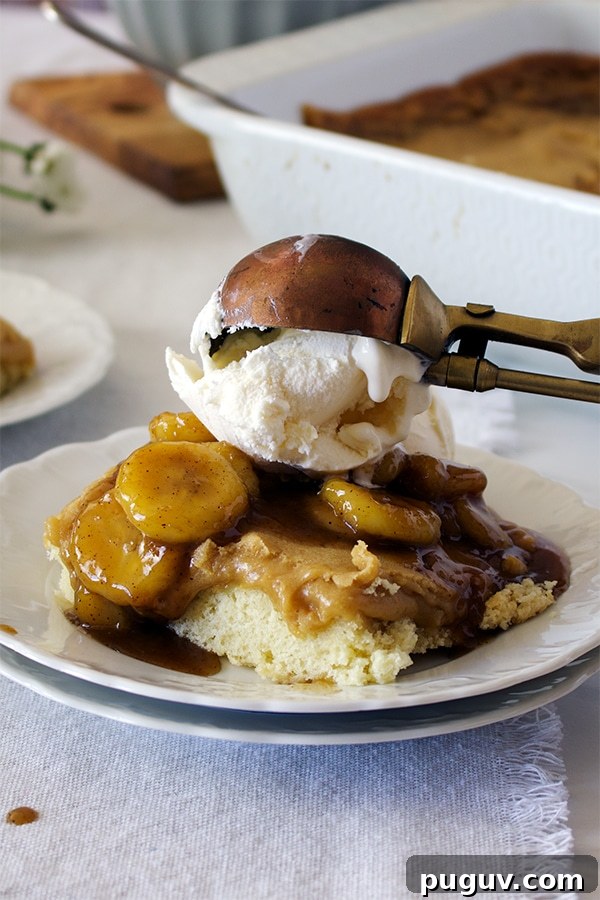 Decadent Bananas Foster Butter Cake Recipe for Dessert Fans 6 Someone using an ice cream scoop to top a piece of Bananas Foster Cake with vanilla ice cream.
