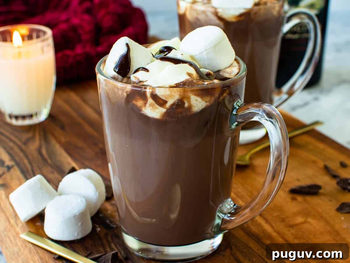 Decadent Baileys Hot Chocolate Recipe for Cozy Nights 6 A clear glass mug filled with hot chocolate topped with marshmallows and cream. A second mug sits behind the first.