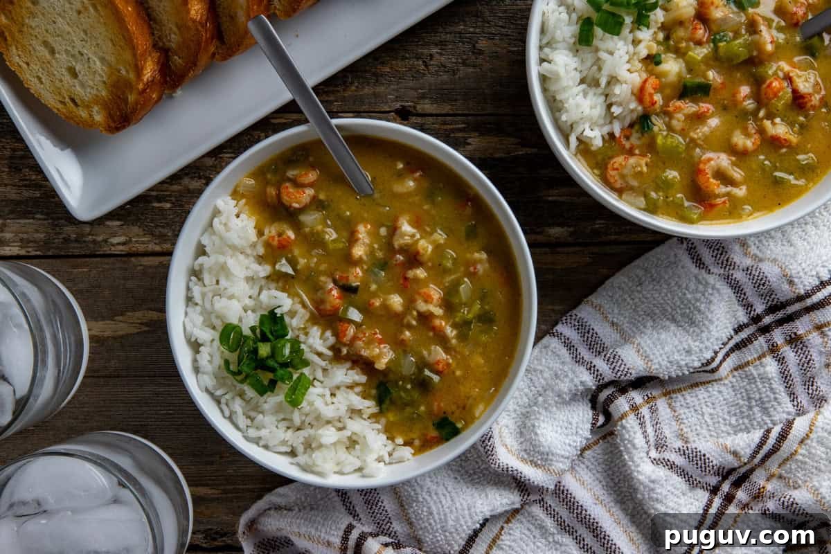 Two bowls of etouffee with white rice. Sliced green onions for garnish. With sliced, toasted French bread in the background.