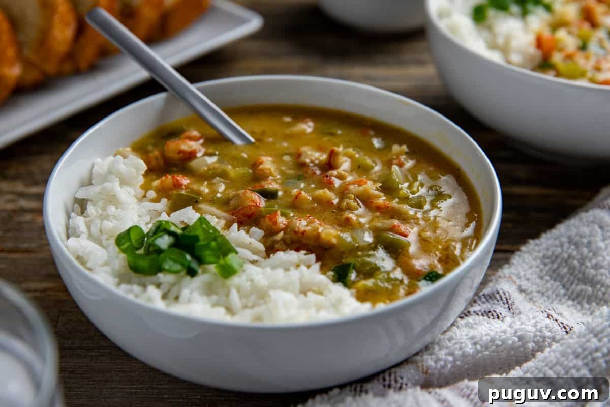 A bowl of etouffee with white rice. Sliced green onions for garnish. With sliced, toasted French bread in the background.