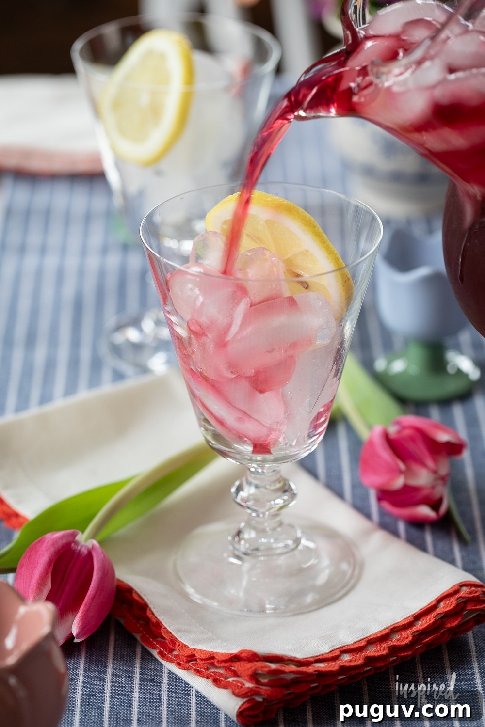 Pink Tulip Cocktail Recipe: Floral Vodka Drink Guide 8 pitcher pouring a tulip cocktail into a glass with ice and a lemon slice.