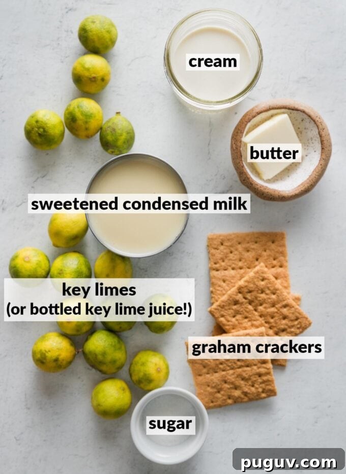 Labeled overhead photo of an open can of sweetened condensed milk, key limes, a pat of butter, granulated sugar, heavy cream, and graham crackers.