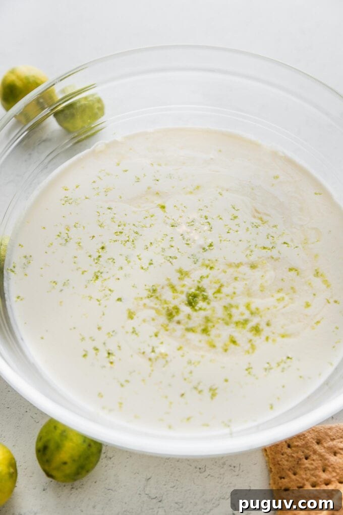 A mixture of sweetened condensed milk and cream in a large bowl, with visible lime zest sprinkled on top.